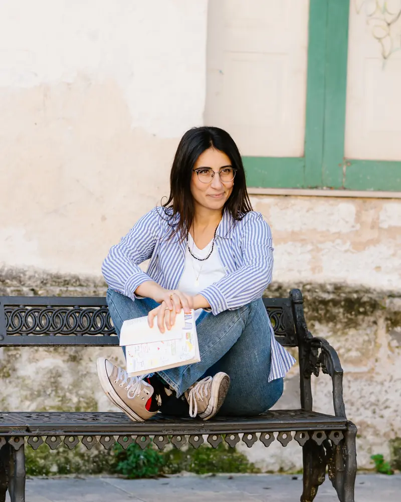 Simona di Punzio seduta su una panchina in ferro battuto, con un quaderno tra le mani