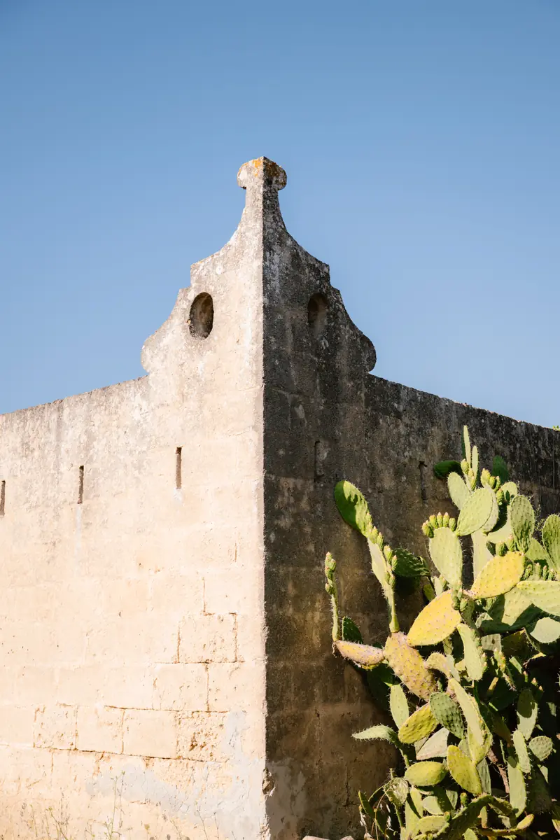 Muro in pietra di un edificio storico con fichi d’India, sotto il cielo azzurro